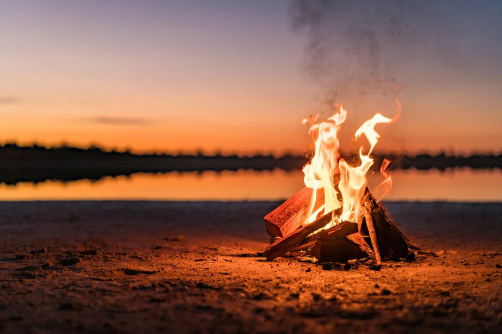 Small campfire with gentle flames beside a lake