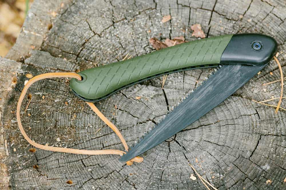 A folding saw lying on a wooden stump.