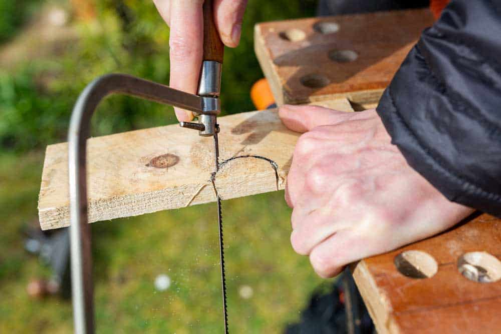 A person using a coping saw to cut a semi-circle out of a plank of wood