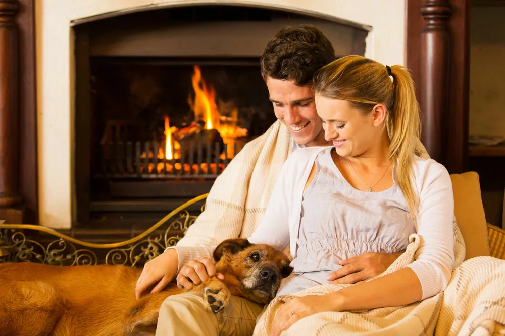 Beautiful young couple sitting by the fireplace with their pet dog. 