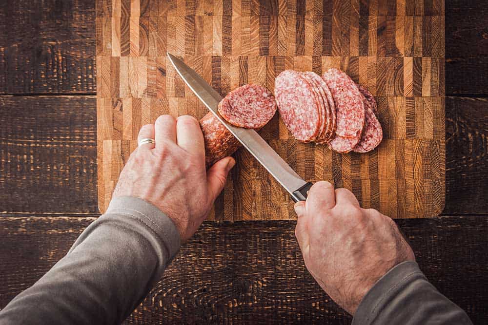 Hands cutting sausage on a wooden board